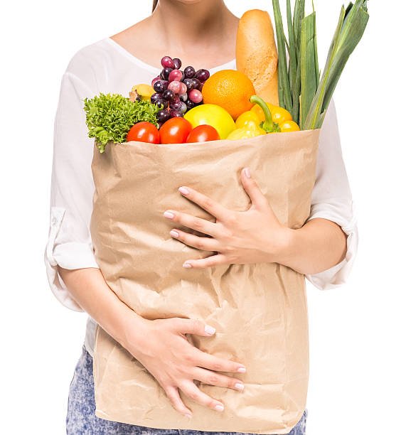 Woman holding shopping bag full of fresh food on white background. Close-up.